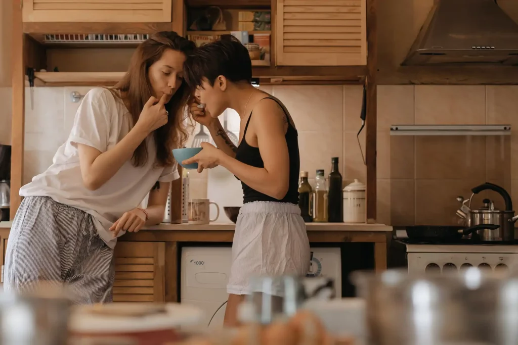 Two women tasting food from a bowl in the kitchen