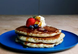A stack of pancakes with berries, cream and syrup